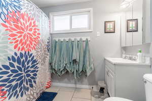 Bathroom with vanity, toilet, curtained shower, and tile patterned flooring