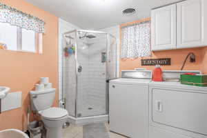 Bathroom with tile patterned floors, a shower with door, washer and dryer, and toilet