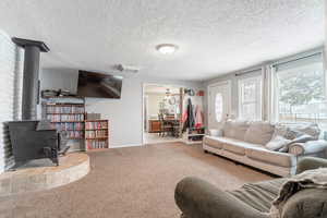 Living room featuring a wood stove, a textured ceiling, ceiling fan, and carpet flooring