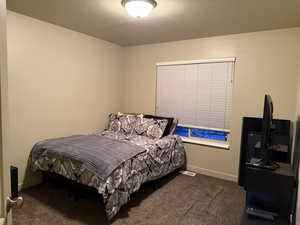 Bedroom with dark carpet and a textured ceiling