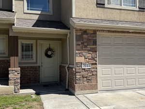 Property entrance with a shingled roof, stucco siding, brick siding, and stone siding