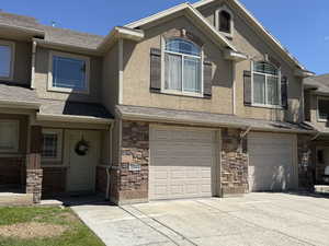 View of property featuring stucco siding, driveway, stone siding, and a garage