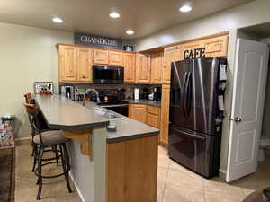 Kitchen with range with electric stovetop, sink, a breakfast bar area, stainless steel fridge, and kitchen peninsula