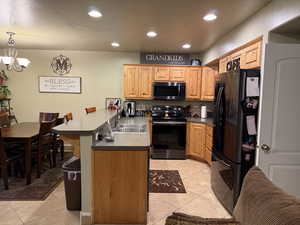 Kitchen featuring stainless steel electric stove, decorative light fixtures, a kitchen breakfast bar, kitchen peninsula, and black refrigerator with ice dispenser