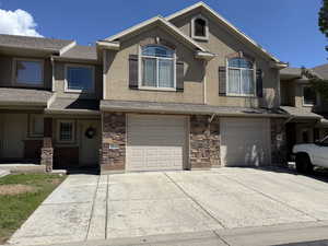 View of property featuring stucco siding, 2 car parking driveway, stone siding, and a garage