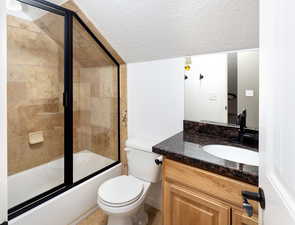 Full bathroom with vanity, enclosed tub / shower combo, toilet, and a textured ceiling