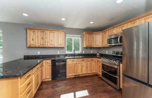 Kitchen with sink, dark stone counters, kitchen peninsula, stainless steel appliances, and dark wood-type flooring