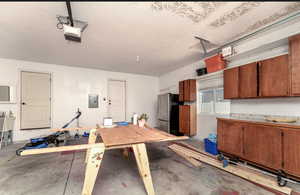 Garage with a garage door opener, electric panel, and stainless steel refrigerator