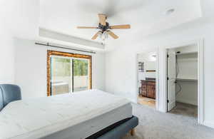 Carpeted bedroom featuring ensuite bath, a spacious closet, a tray ceiling, ceiling fan, and access to exterior