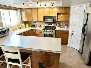 Kitchen with sink, appliances with stainless steel finishes, a kitchen breakfast bar, kitchen peninsula, and decorative backsplash