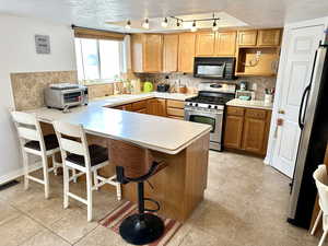 Kitchen with sink, appliances with stainless steel finishes, a kitchen breakfast bar, kitchen peninsula, and backsplash