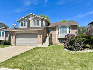 Tri-level home with brick siding, an attached garage, driveway, a front lawn, and a shingled roof