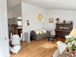 Living room with lofted ceiling, radiator, and light wood-type flooring