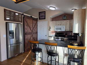 Kitchen with appliances with stainless steel finishes, lofted ceiling, dark hardwood / hardwood flooring, a kitchen breakfast bar, and a barn door