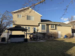 Rear view of house featuring a hot tub, a gazebo, a patio, and a lawn