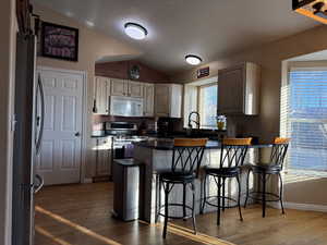 Kitchen with lofted ceiling, a kitchen bar, appliances with stainless steel finishes, kitchen peninsula, and hardwood flooring