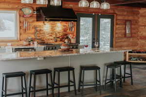Kitchen with log walls, range hood, french doors, and light stone counters