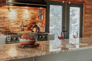 Kitchen with rustic walls, under cabinet range hood, french doors, range, and light stone counters