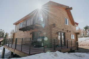 View of snow covered exterior featuring french doors, log siding, and a balcony