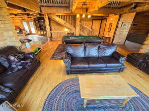 Living room with hardwood / wood-style flooring, beamed ceiling, pool table, and rustic walls