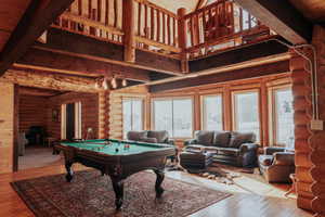 Game room with pool table, a towering ceiling, rustic walls, beam ceiling, and wood finished floors