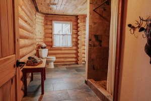 Bathroom featuring a shower stall, toilet, wood ceiling, log walls, and stone tile flooring