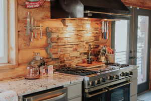 Kitchen featuring backsplash, under cabinet range hood, light stone counters, and stainless steel appliances