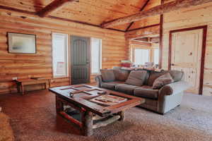 Living room featuring vaulted ceiling with beams, log walls, carpet, and wooden ceiling
