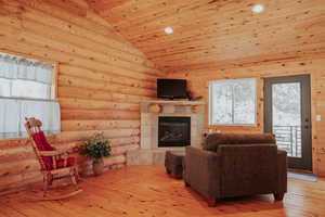 Living room featuring wooden ceiling, rustic walls, light wood finished floors, a tile fireplace, and lofted ceiling