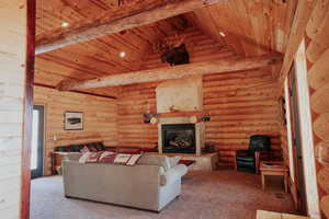 Carpeted living area featuring beamed ceiling, a stone fireplace, wooden ceiling, and rustic walls