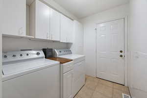 Washroom with tile walls, washing machine and clothes dryer, light tile patterned floors, and cabinets