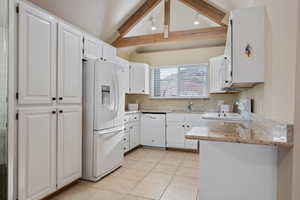 Kitchen with white appliances, vaulted ceiling with beams, white cabinets, and light counters