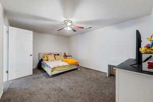 Carpeted bedroom with ceiling fan and a textured ceiling