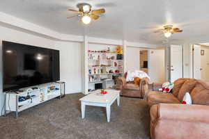 Living room with a textured ceiling, dark colored carpet, and ceiling fan