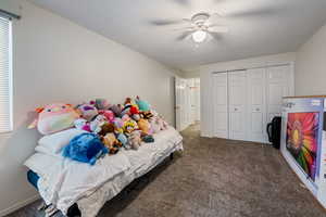 Carpeted bedroom with ceiling fan and a closet