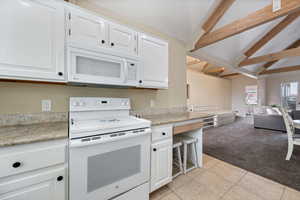 Kitchen featuring white cabinets, white appliances, lofted ceiling