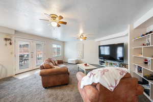 Living room featuring ceiling fan, light carpet, french doors, and a textured ceiling