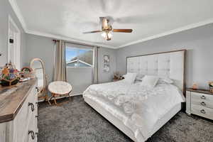 Bedroom with ceiling fan, ornamental molding, a textured ceiling, and dark colored carpet