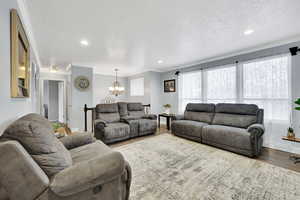 Living room with hardwood / wood-style flooring, crown molding, a textured ceiling, and an inviting chandelier