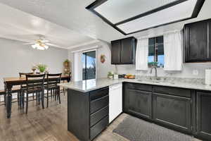 Kitchen featuring dishwasher, sink, light wood-type flooring, kitchen peninsula, and a textured ceiling