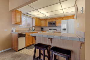 Kitchen featuring light tile patterned flooring, a breakfast bar, sink, tile counters, and white appliances