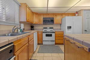 Kitchen with light tile patterned flooring, white appliances, tile counters, and sink