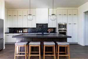 Kitchen featuring white cabinetry, dark hardwood / wood-style flooring, a kitchen island with sink, and stainless steel appliances