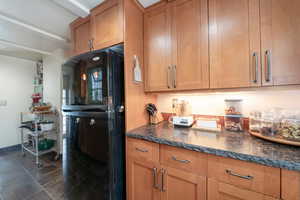 Kitchen featuring black fridge, dark tile patterned flooring, and dark stone countertops