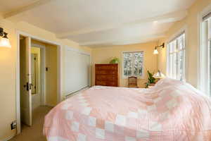 Carpeted bedroom with beamed ceiling and a closet