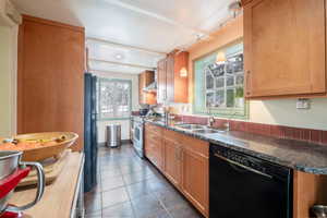 Kitchen with pendant lighting, sink, dark tile patterned floors, black appliances, and wall chimney range hood