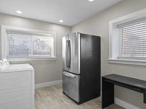 Laundry with stainless steel fridge, washing machine and clothes dryer, and light wood-type flooring