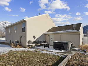 Snow covered back of property with a mountain view, central AC, a hot tub, and a patio