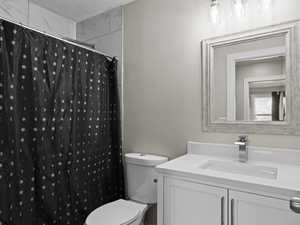 Bathroom featuring a shower with curtain, vanity, a textured ceiling, and toilet