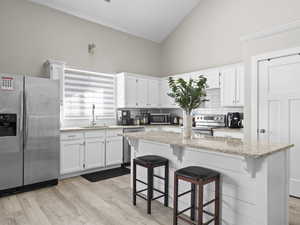 Kitchen featuring a kitchen bar, white cabinetry, a center island, appliances with stainless steel finishes, and light stone countertops